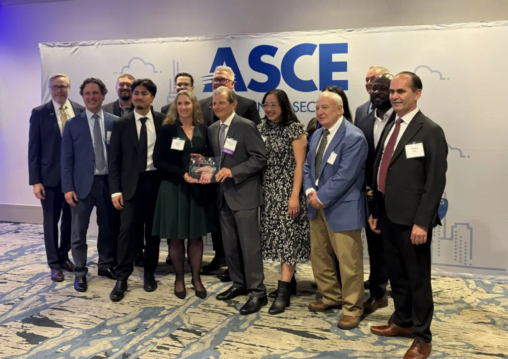 Group of professionals posing at an ASCE event, with two people holding an ASCE award in front of the event backdrop