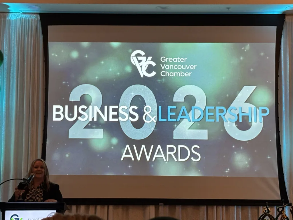 Speaker at a podium beside a screen displaying “Greater Vancouver Chamber” and “BUSINESS & LEADERSHIP AWARDS 2023.”