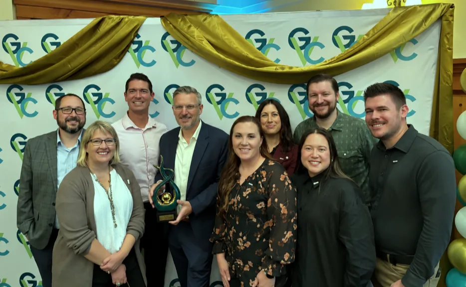 Group of nine people posing with an award in front of a branded event backdrop