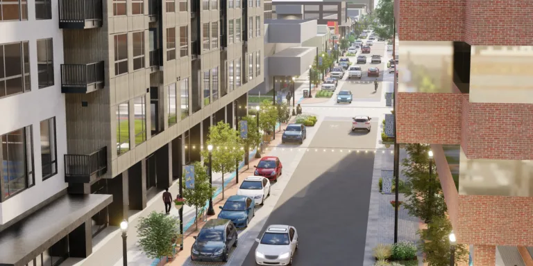 3D rendering of a modern downtown street with mid-rise buildings, trees, lampposts and string lights, angled street parking, a bike symbol on the roadway, and pedestrians on wide sidewalks.