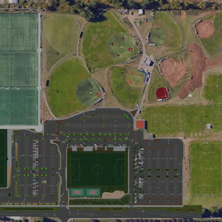 Aerial view of a large sports complex with multiple soccer fields (turf and grass), a cluster of baseball/softball diamonds, extensive central parking lots, and surrounding roads and trees.