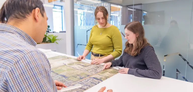 MacKay team reviewing a large aerial site plan together in a bright, modern office with glass walls.