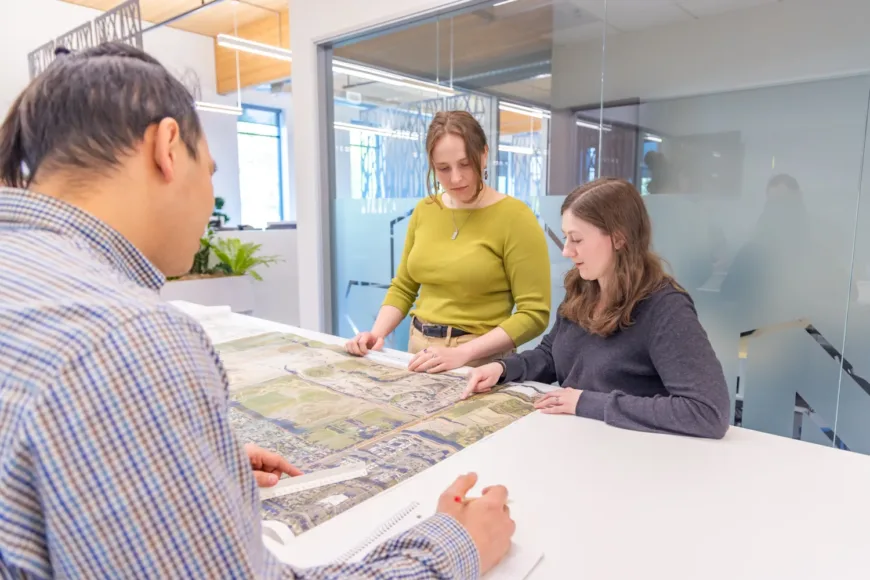 MacKay team reviewing a large aerial site plan together in a bright, modern office with glass walls.