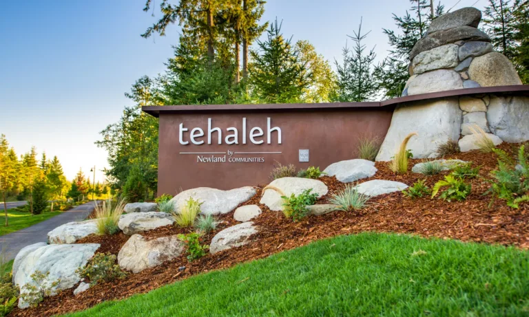 Entrance monument sign reading “tehaleh by Newland Communities,” surrounded by landscaped rocks and greenery with evergreen trees in the background.