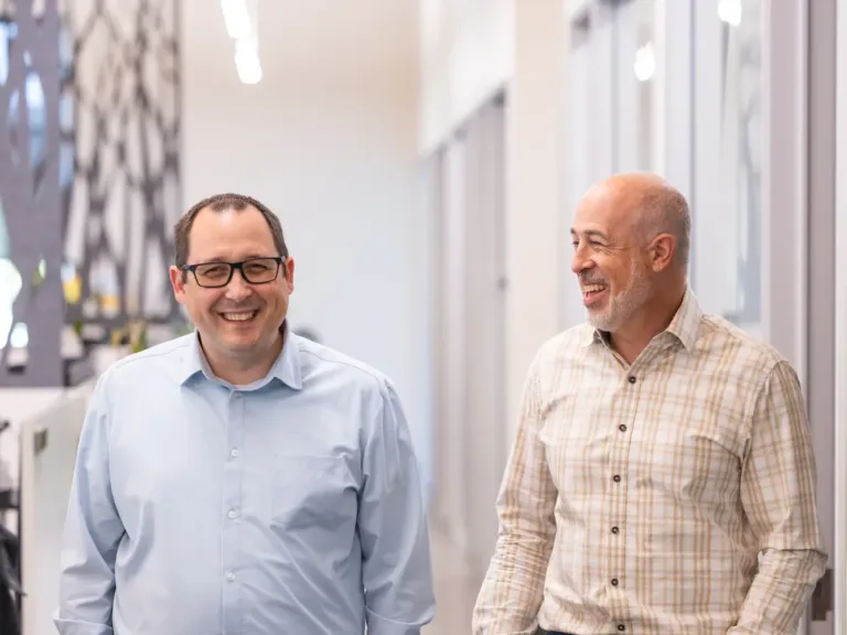 Two MacKay team members smile while walking down a bright, modern office hallway.