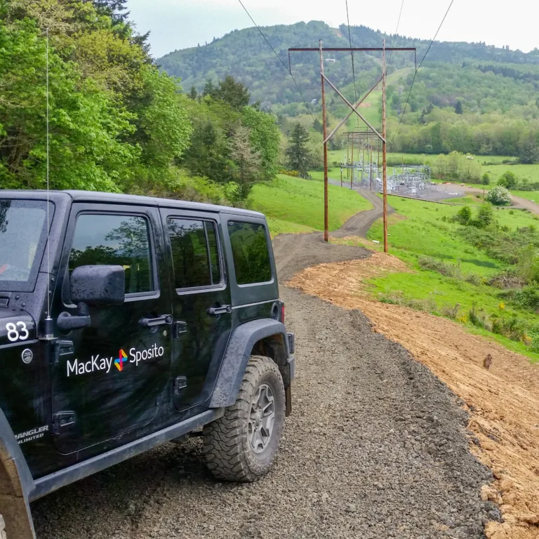 Jeep with company logo driving up gavel road with greenery in the background