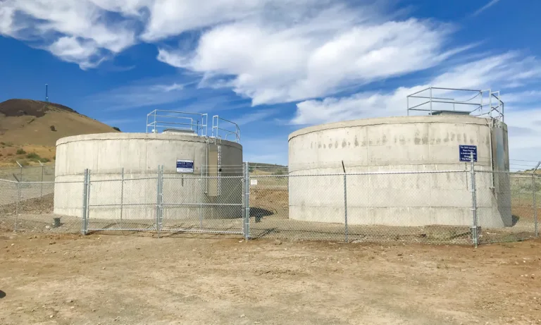 Two concrete water storage tanks labeled “Baker Silo” behind a chain-link fence in a dry, hilly landscape