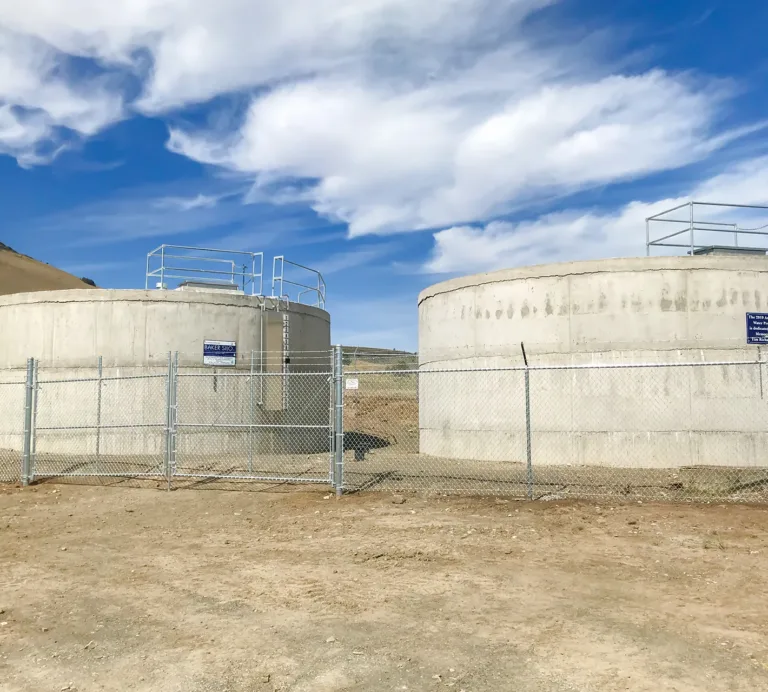 Two concrete water storage tanks labeled “Baker Silo” behind a chain-link fence in a dry, hilly landscape