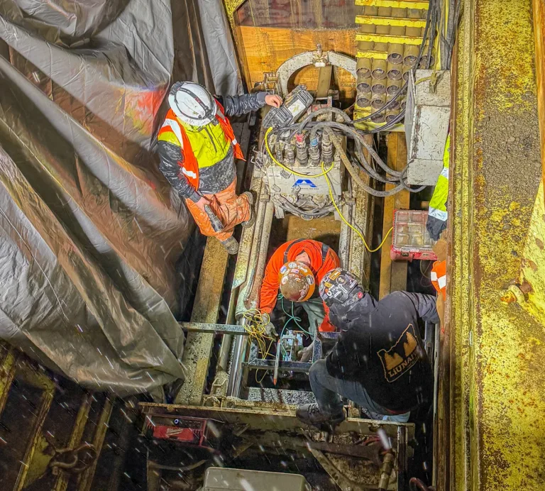Workers in high-visibility safety gear operate heavy machinery inside a confined industrial space