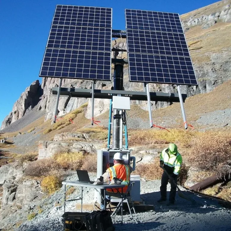 Workers inspect a solar panel installation on a rocky mountainside