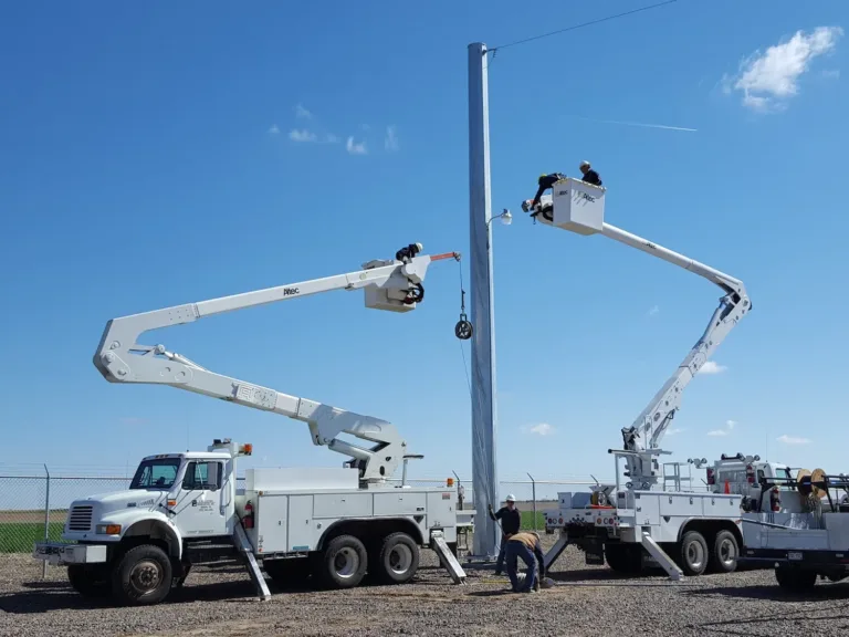 Utility crews use bucket trucks to install a tall electrical pole at a substation