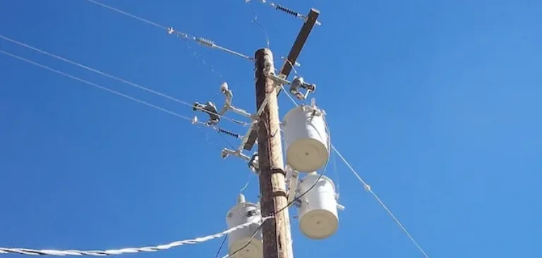 Utility pole with multiple transformers and overhead power lines against a clear blue sky