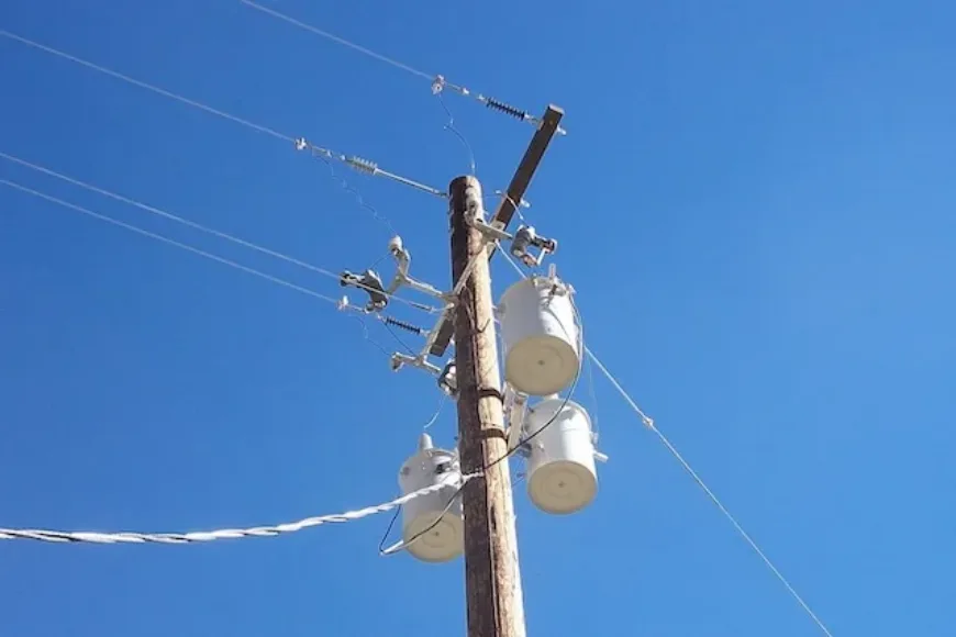 Utility pole with multiple transformers and overhead power lines against a clear blue sky