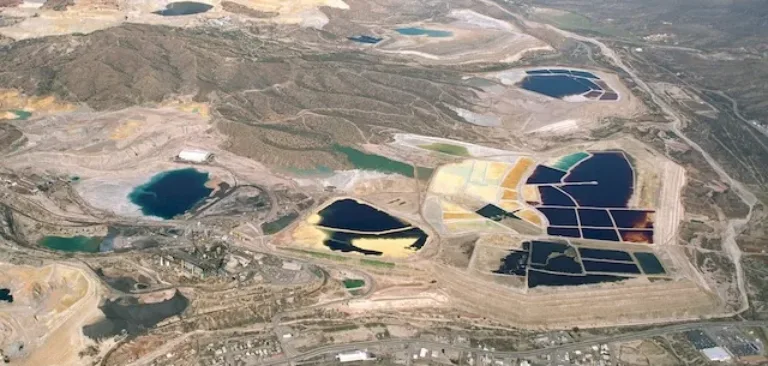 Aerial view of a mining site with colorful tailings ponds and a residential area along its edge
