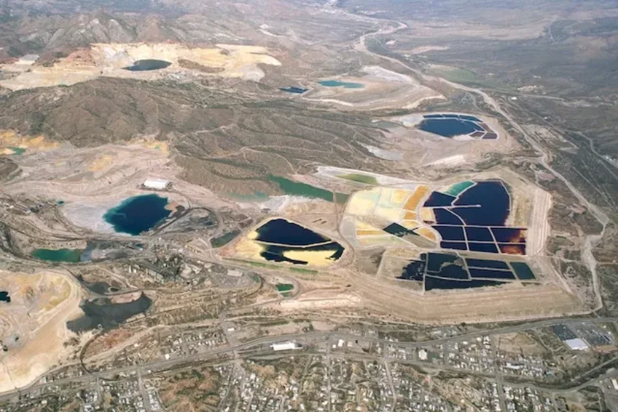 Aerial view of a mining site with colorful tailings ponds and a residential area along its edge