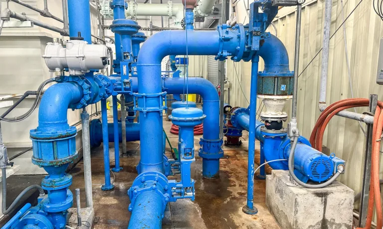 Industrial pump system with large blue pipes, valves, gauges, and motors inside a mechanical equipment room
