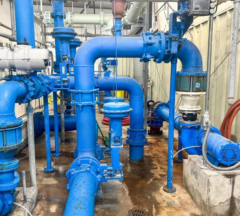 Industrial pump system with large blue pipes, valves, gauges, and motors inside a mechanical equipment room