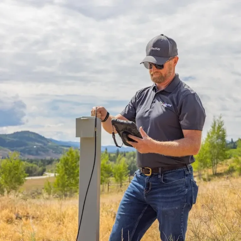 Technician using a handheld device to inspect a utility box in a rural field