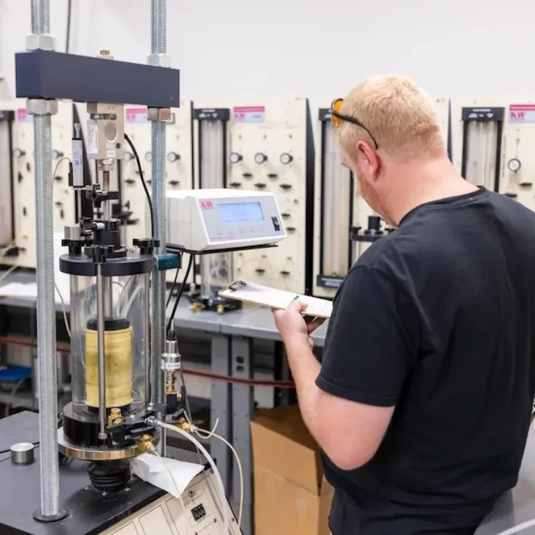 Technician records measurements beside a laboratory soil testing apparatus