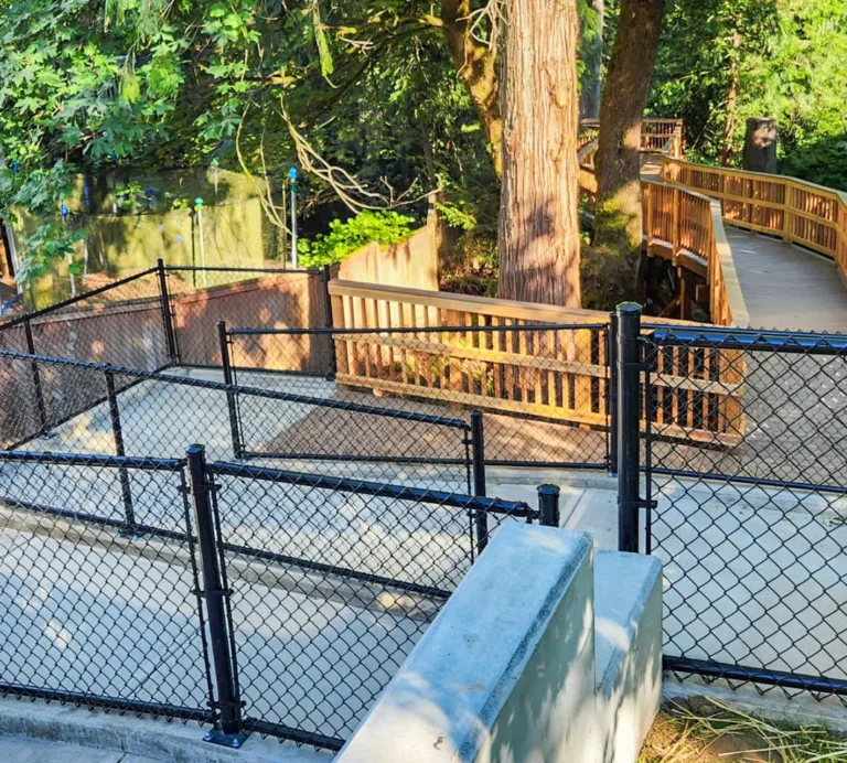 Accessible wooden boardwalk winding through a wooded area beside a fenced concrete walkway