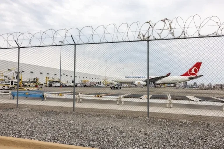 Turkish Cargo airplane parked on the airport tarmac behind a chain-link fence topped with razor wire