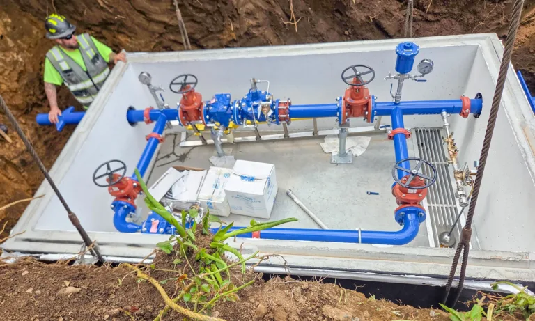 Worker installs blue and red water pipes and valves inside a concrete utility vault