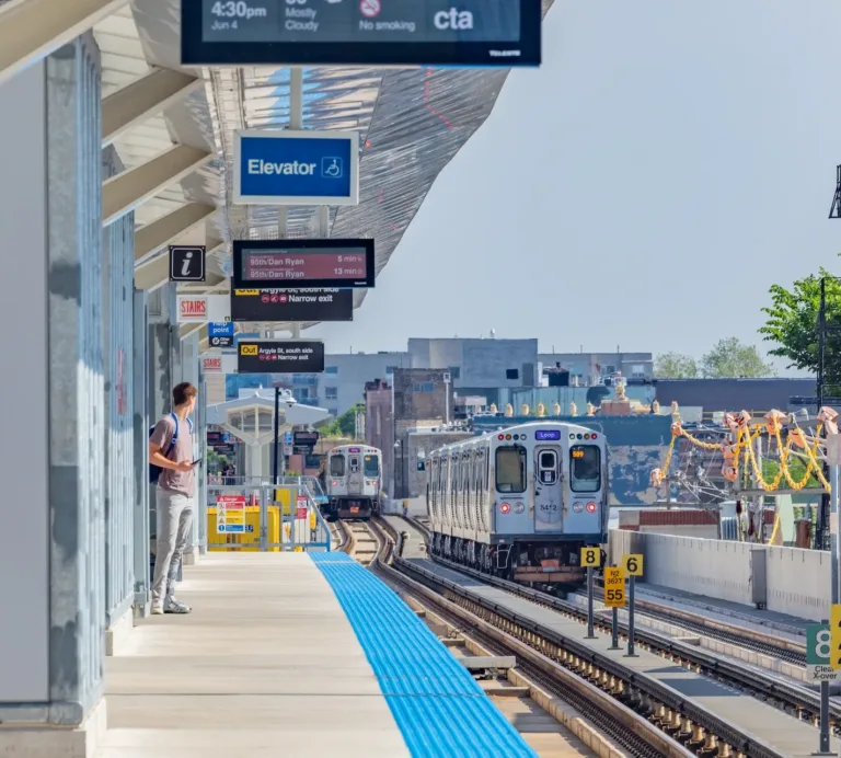 CTA elevated train station platform with two trains, accessibility and direction signs, and a passenger waiting