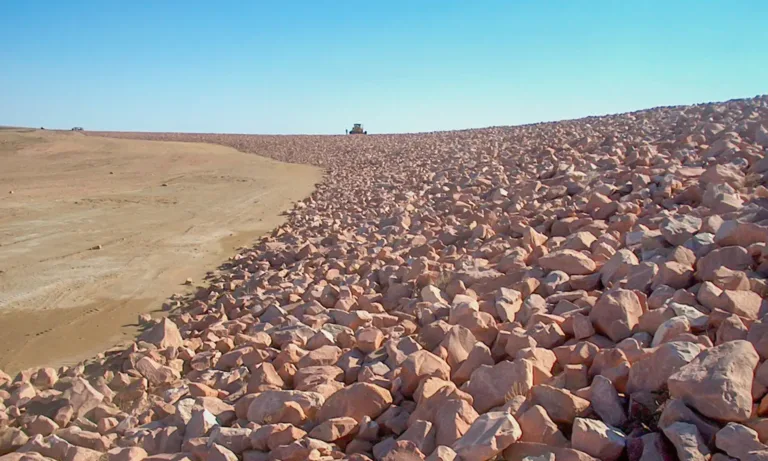 Rock-covered embankment beside a barren dirt slope under a clear blue sky