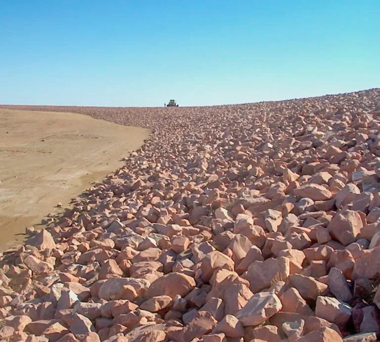 Rock-covered embankment beside a barren dirt slope under a clear blue sky