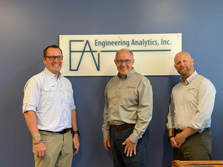 Three men pose beneath a sign reading “Engineering Analytics, Inc.”