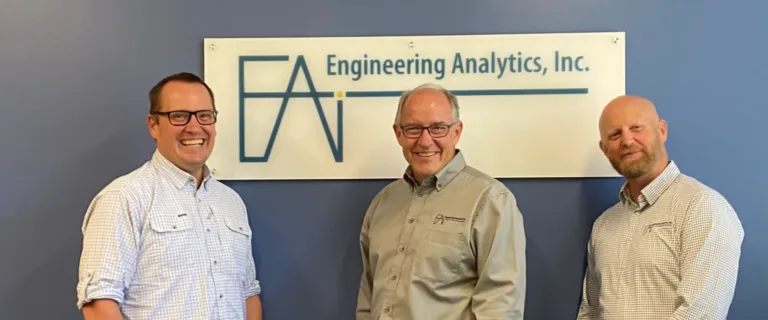 Three men pose beneath a sign reading “Engineering Analytics, Inc.”