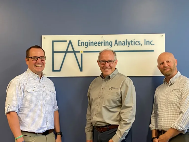 Three men pose beneath a sign reading “Engineering Analytics, Inc.”