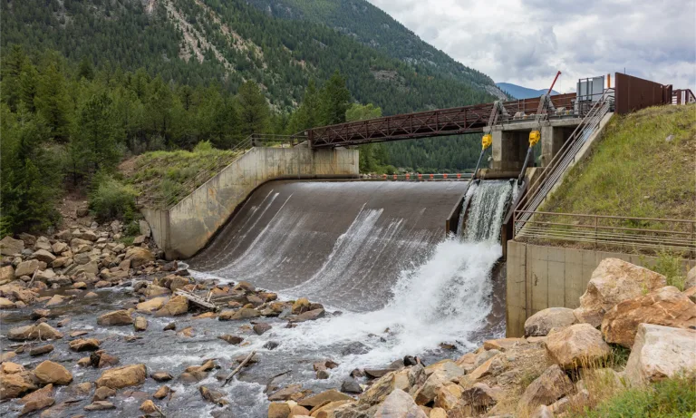 Small hydroelectric dam releasing water into a rocky stream in a forested mountain valley