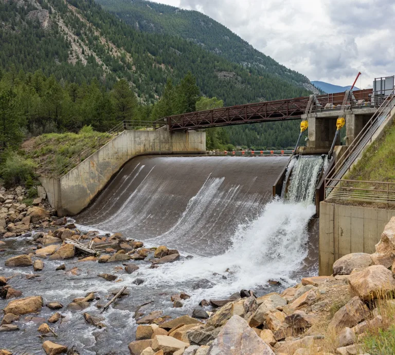 Small hydroelectric dam releasing water into a rocky stream in a forested mountain valley
