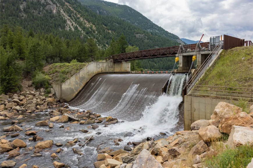Small hydroelectric dam releasing water into a rocky stream in a forested mountain valley