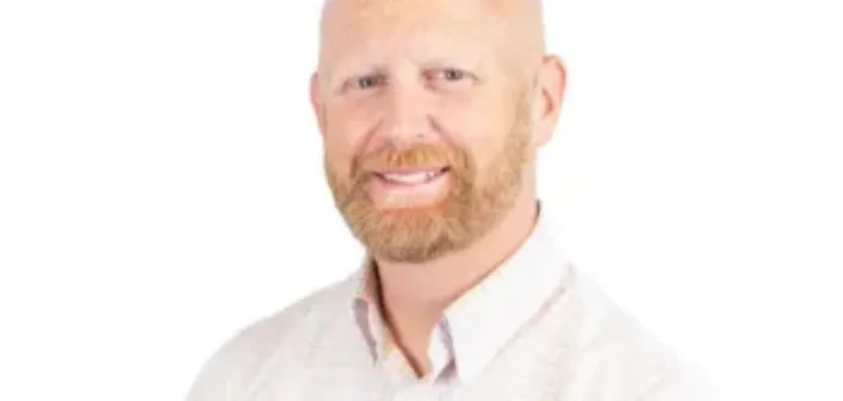 Smiling bald man with a reddish beard wearing a light plaid button-down shirt