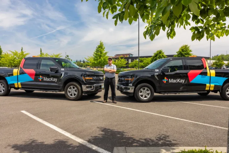 A man stands between two branded MacKay pickup trucks numbered 118 and 114