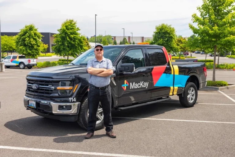 Man standing with folded arms beside a branded Ford pickup truck in a parking lot