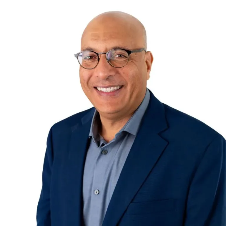 Smiling bald man wearing glasses, a blue blazer, and a gray collared shirt