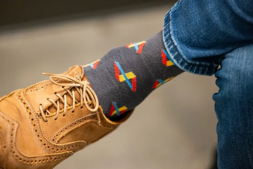 Close-up of a tan leather brogue shoe, colorful patterned sock, and blue jeans