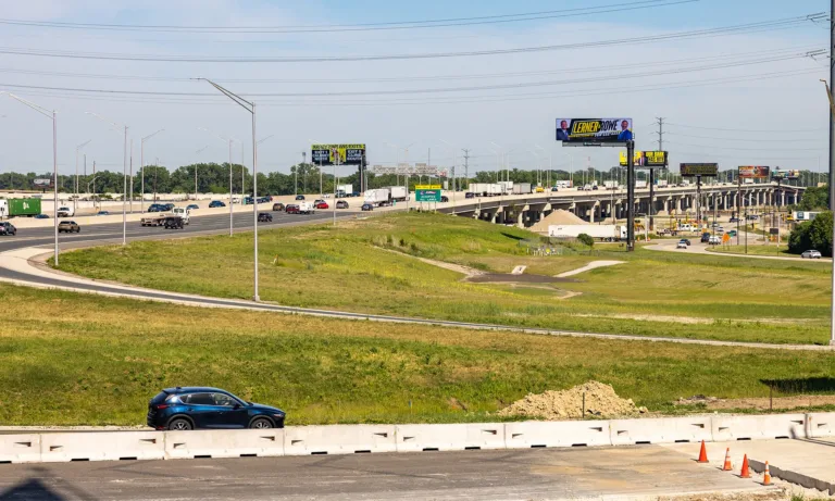 Multilane highway interchange with traffic, overpasses, billboards, and construction barriers