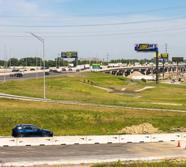 Multilane highway interchange with traffic, overpasses, billboards, and construction barriers