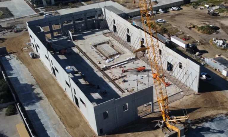 Aerial view of a large commercial building under construction, with concrete walls, construction equipment, and a tower crane