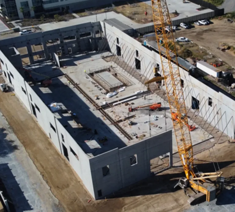 Aerial view of a large commercial building under construction, with concrete walls, construction equipment, and a tower crane