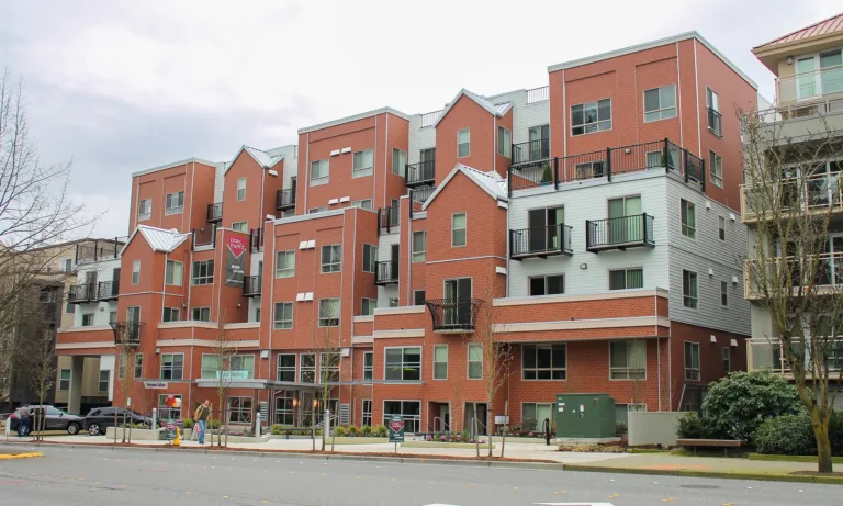 Apartment building with red brick and gray siding, balconies, street-level shops, and “park metro NOW LEASING” signs