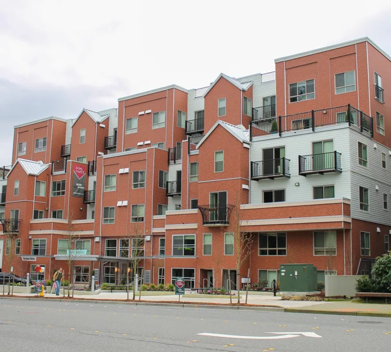 Apartment building with red brick and gray siding, balconies, street-level shops, and “park metro NOW LEASING” signs