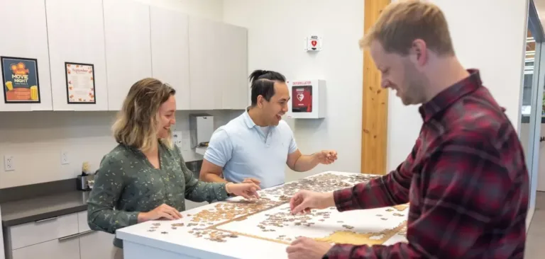 Three people assemble a jigsaw puzzle together around a kitchen island