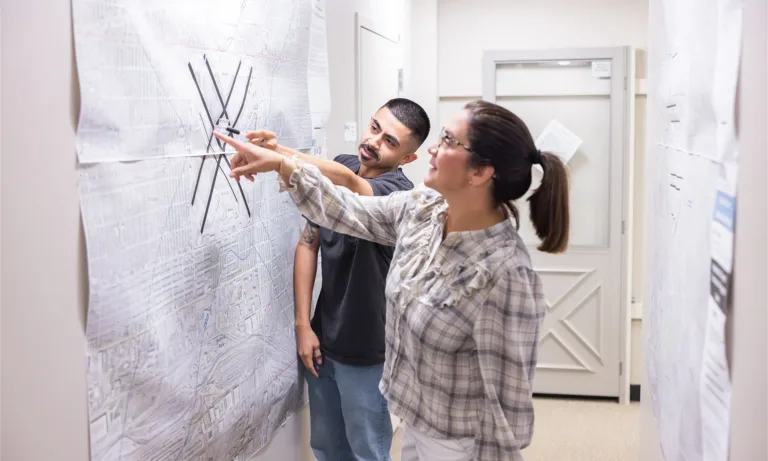 Two people point to locations on a large wall map
