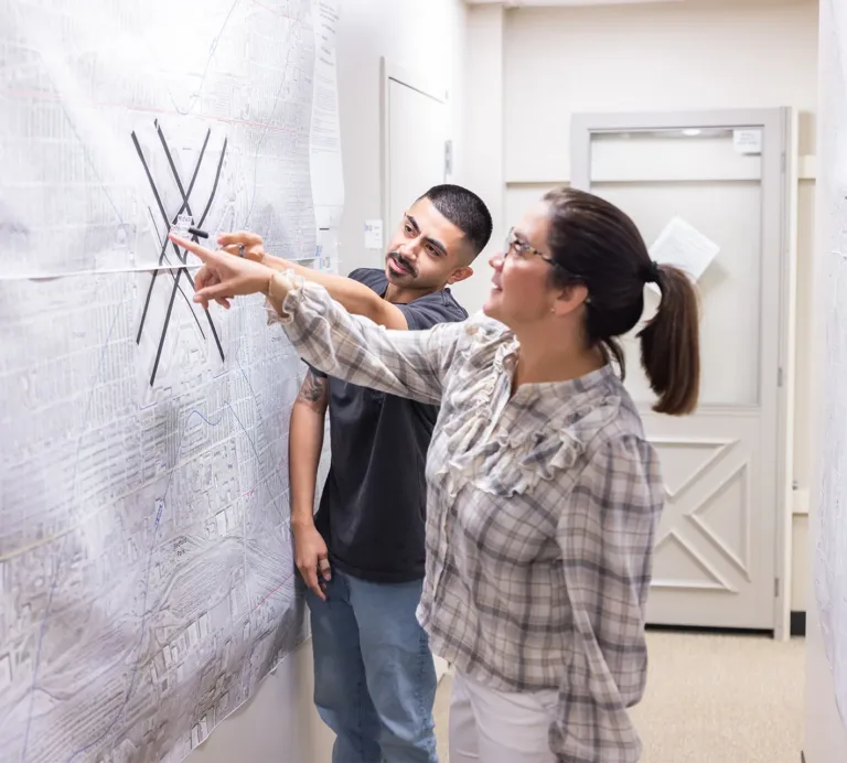 Two people point to locations on a large wall map