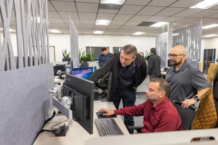 Three coworkers collaborate at a computer workstation in an open-plan office
